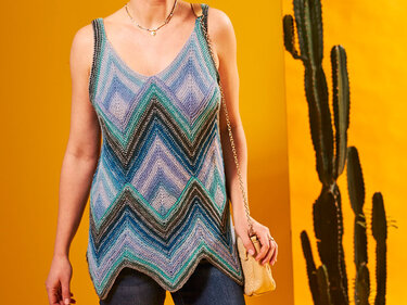 Gestricktes Damen-Top mit V-Ausschnitt und blau-türkisfarbenem Zickzackmuster vor gelbem Hintergrund mit Kakteen