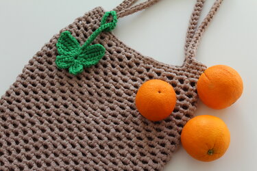 Beige gehäkelte Netztasche mit offenem Netzmuster, grüner Blatt-Applikation und drei Orangen