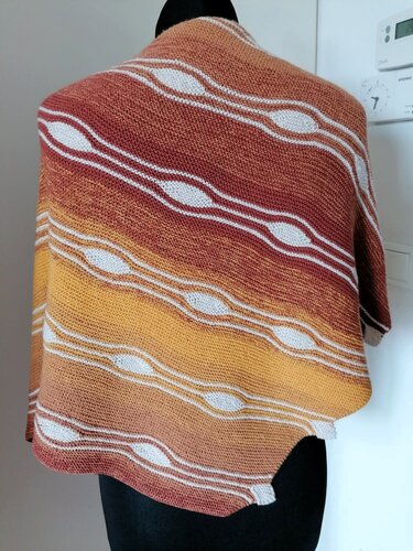 Gestricktes Dreieckstuch in Terracotta- und Gelbtönen mit weißen wellenförmigen Mustern auf einer Schneiderpuppe.
