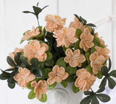 Bouquet aus apricotfarbenen gehäkelten Blumen mit grünen Blättern in weißer Vase