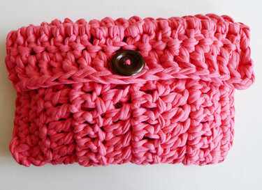 Pinkfarbene gehäkelte Clutch mit rundem braunem Knopf auf hellem Hintergrund