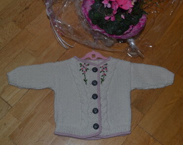hellbeige gestrickte Babyjacke mit Blumenstickerei und dunklen Knöpfen auf Holzboden