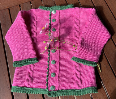 Gestrickte Kinderjacke in Pink mit grünen Abschlüssen und Knöpfen, flach gelegt