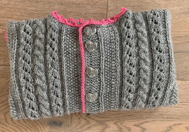 Grau gestrickte Kinderjacke mit Zopfmustern, pinker Borte und herzförmigen Knöpfen