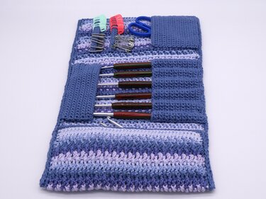 Gehäkelte Nadelrolle in Blau-Lila offen mit Häkelnadeln, Schere und Maschenmarkierern