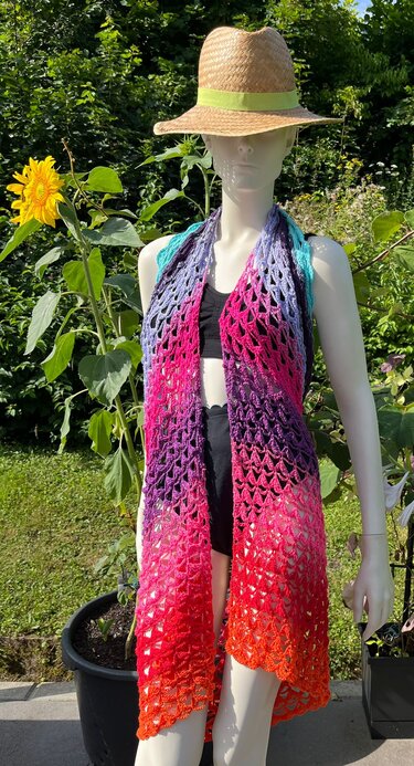Mannequin im Garten trägt bunten Häkelüberwurf mit Farbverlauf über schwarzem Top und Strohhut