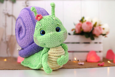 Plush-textured green amigurumi snail with purple spiral shell and ridged belly
