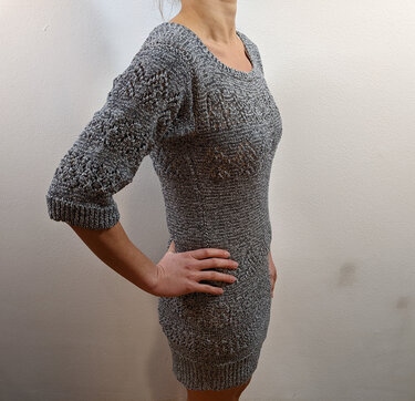 Frau in eng anliegendem grauen Strickkleid mit Dreiviertelärmeln und feinem Lochmuster