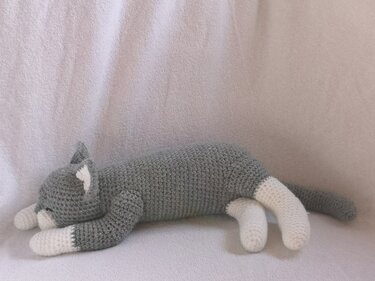 Grey and white crocheted amigurumi cat lying on its side, sleeping
