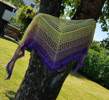 Gehäkeltes Dreieckstuch in Gelb–Lila mit Spitzenmuster, an einem Baumstamm drapiert