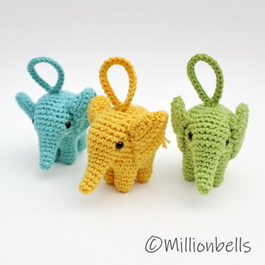 Three small crocheted elephant keychains in teal, yellow and green with hanging loops on a white background