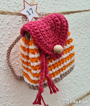 Striped orange and white crochet pouch with pink flap, wooden bead closure, and braided cord, hung on twine with star tag '17'.