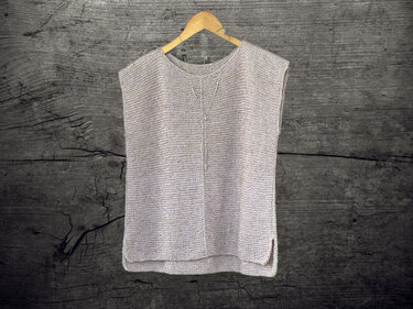 Neutral sleeveless knitted top with central V-stitch and side slits on a wooden hanger