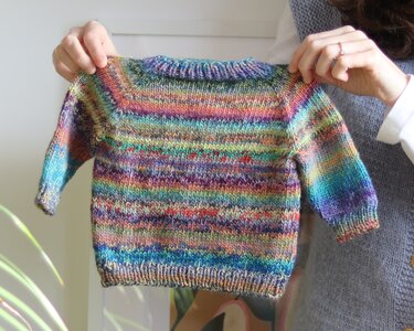 Hands holding a small multi-colored knitted baby sweater with long sleeves.