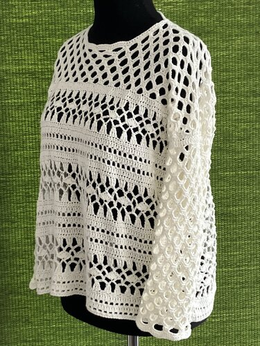 Weiße gehäkelte Tunika mit verschiedenen Lochmustern auf Büste vor grünem Hintergrund