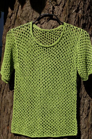 limettengrüner, ajourgestrickter Kurzarm-Pullover an Kleiderbügel vor Baumrinde