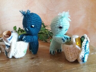 Zwei gehäkelte Amigurumi-Figuren (dunkelblau und mint) mit kleinen gehäkelten Täschchen auf Holzbrett