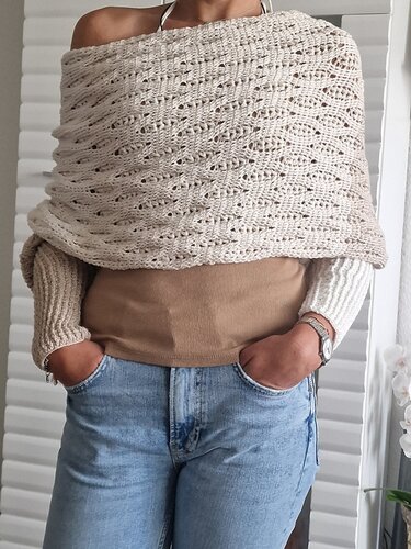 Beiger gehäkelter Wickelschal mit Lochmuster über beigem Top und blauen Jeans.