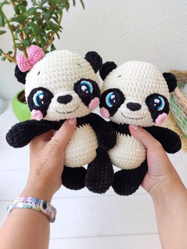 Two small crochet panda amigurumi held in hands showing black markings and a pink bow on one