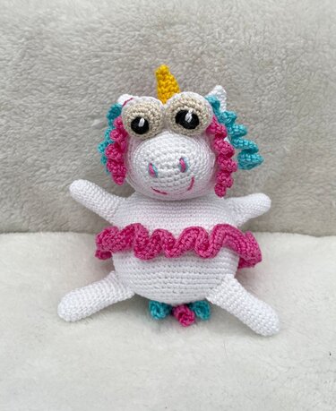 Weißes gehäkeltes Einhorn-Amigurumi mit gelbem Horn, pink-türkiser Lockenmähne und pinkem Rüschenrock