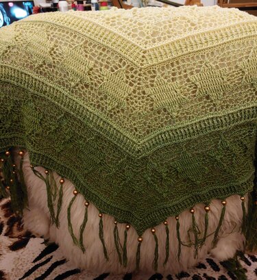 Ombre green crochet triangle shawl with lace stitches and beaded tassels on white faux fur.