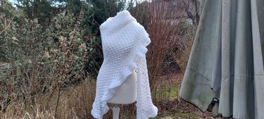 weißes gehäkeltes Dreieckstuch mit Rüschen auf Schaufensterpuppe vor winterlichem Garten