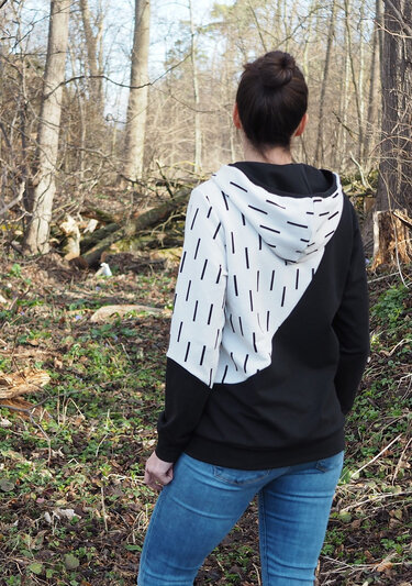 Rückenansicht eines Hoodies mit diagonaler weißen Passe mit kurzen schwarzen Strichen und schwarzem Grundstoff, Kapuze