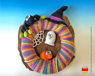Farbenfroher, gehäkelter Halloween-Türkranz mit gestreiftem Muster, dekoriert mit Hexe, Spinne, weißem Geist und orangenem Kürbis auf Holzuntergrund