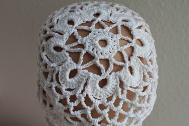 Weiße gehäkelte Damenmütze mit Blumenmotiven und Netzstruktur auf Kopfmodell