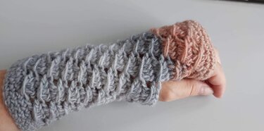 Hand mit gehäkelter, fingerloser Armstulpe grau und rosé Bündchen