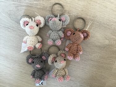 Fünf gehäkelte Amigurumi-Mäuse als Schlüsselanhänger in Pastellfarben auf hellem Holz
