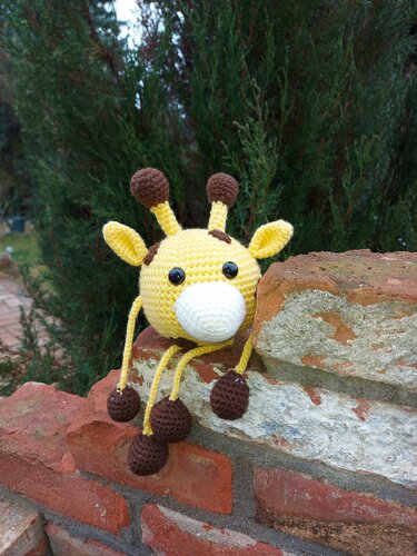 Gelbes gehäkeltes Giraffen-Amigurumi mit braunen Details auf Ziegelmauer
