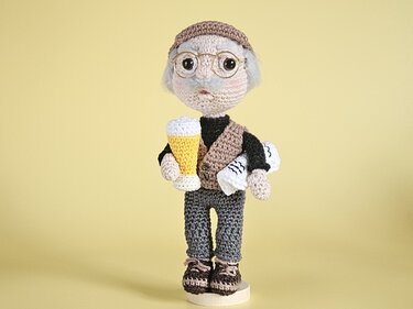 Gehäkelte Puppe eines älteren Mannes mit Brille, Mütze, Weste, Bierglas und gerollten Papieren