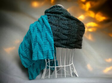 Two crocheted scarves, teal and dark grey, with a basketweave texture draped over a white wire mannequin.