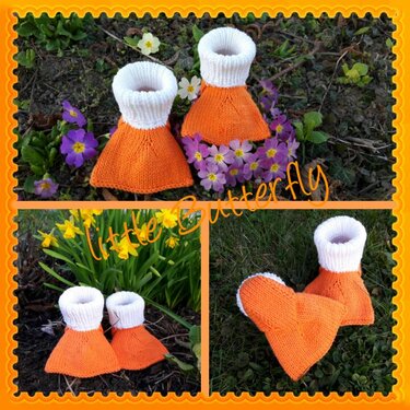 Ein Paar gestrickte Babyschühchen in Orange und Weiß auf grüner Wiese mit Frühlingsblumen.