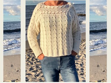 Person am Strand in lässigem cremefarbenen gehäkelten Pullover mit Zopfmuster