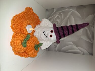 Gehäkelte Halloween-Tischdeko mit weißem Geist, violett-schwarz gestreiftem Hexenhut, orangefarbener Kürbis-Häkelunterlage mit grünen Details und kleinem elektrischem Teelicht.