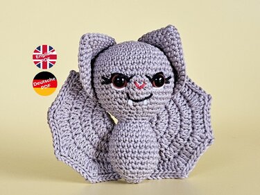 Gehäkelte graue Amigurumi-Fledermaus mit ausgebreiteten Flügeln und großen Augen auf hellem Hintergrund