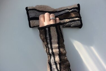 Gestrickte gestreifte Armstulpe in Beige, Braun und Schwarz an einer Hand.