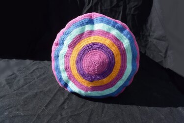Runde gehäkelte Umhängetasche mit konzentrischen Streifen in Pink, Violett, Gelb, Türkis und Hellblau auf dunklem Hintergrund