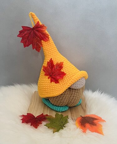 Gehäkelter Herbstwichtel mit gelber Spitzmütze und roten Ahornblättern