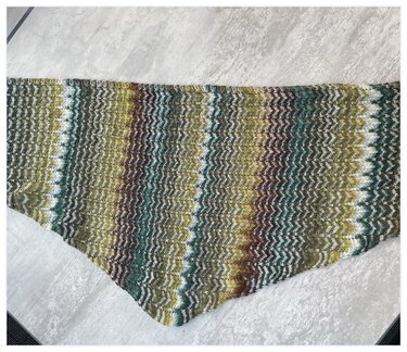 Gestricktes Dreieckstuch mit wellenförmigem Zickzack-Muster in Grün-, Braun- und Weißtönen auf hellem Untergrund.