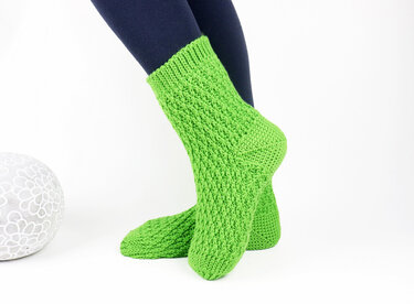 Leuchtend grüne gehäkelte Socken mit feinem Strukturmuster, getragen vor weißem Hintergrund.
