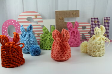 Sechs gehäkelte Hasenbeutel in Orange, Blau, Grün, Lachs, Pink und Creme mit Ohren und Zugband.