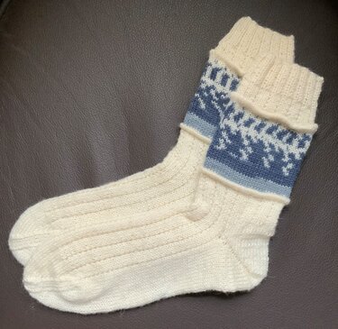 Cremefarbene Stricksocken mit blauem Fair‑Isle‑Muster am Bündchen auf dunklem Untergrund