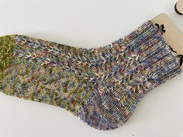 Mehrfarbige handgestrickte Socke mit Strukturmuster auf hellem Hintergrund.