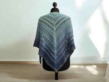 Blue-green ombre crochet triangle shawl draped on a black mannequin