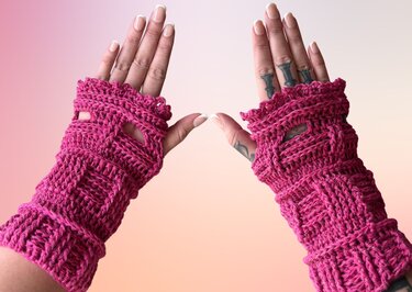Zwei Hände mit pinken, gehäkelten, fingerlosen Handschuhen; Daumenöffnungen sichtbar