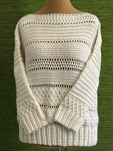Cremefarbener gehäkelter Damenpullover mit langen Ärmeln auf einer Schneiderpuppe vor grünem Hintergrund.