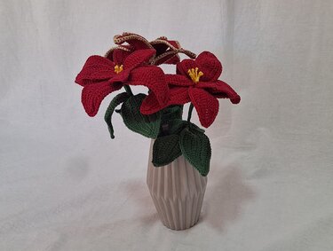 Red crocheted poinsettia flowers with green leaves in a tall ribbed vase
